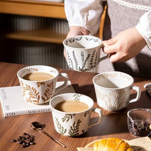 Person holding decorative coffee mug with more on table