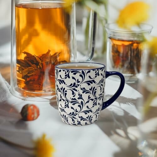 Floral tea cup on table with glass teapots in sunlight.