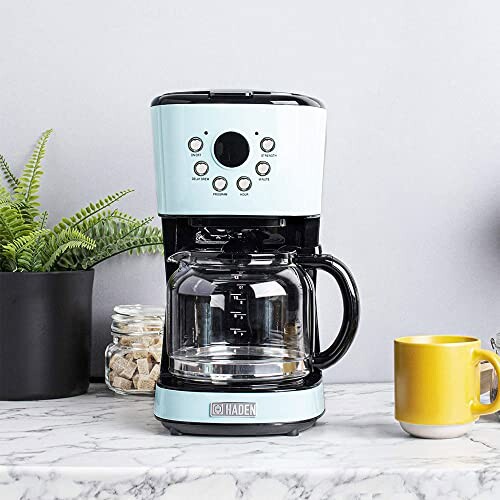 Modern coffee maker on a kitchen counter with plants and mugs.