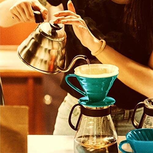 Person making pour-over coffee with a kettle and dripper.