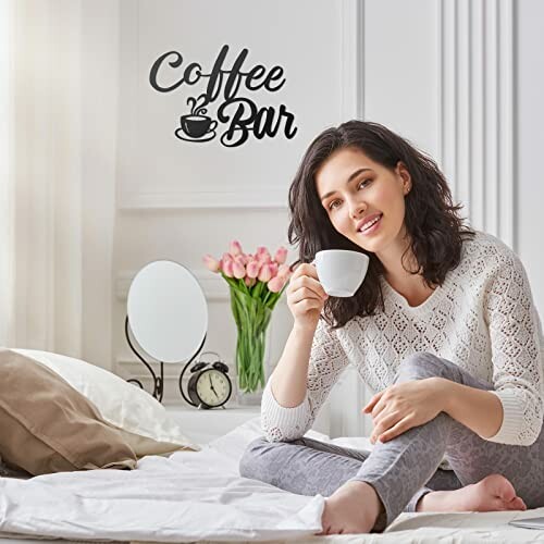 Woman sitting on bed with coffee cup and decor items in background.