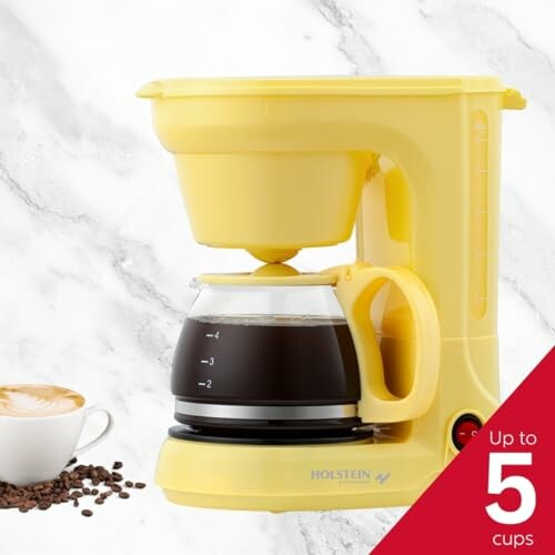 Yellow coffee maker with a cup of coffee on marble background.